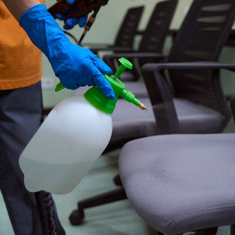 Empleado rociando producto de limpieza en sillas de oficina